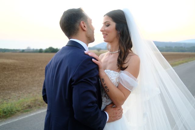 Bride and groom embracing on a rural road during sunset, capturing a romantic wedding moment.